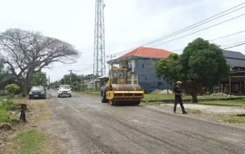 Alat berat perata jalan bekerja di salah satu ruas jalan kabupaten Pinrang sementara beberapa kendaraan melintas di sisi kiri dan kanan jalan