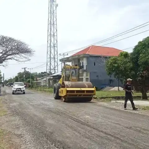 Alat berat perata jalan bekerja di salah satu ruas jalan kabupaten Pinrang sementara beberapa kendaraan melintas di sisi kiri dan kanan jalan