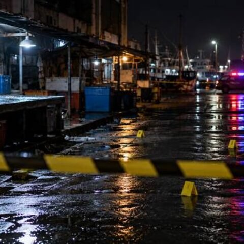 Area pasar kosong pada malam hari dengan garis polisi dan lampu kendaraan di kejauhan